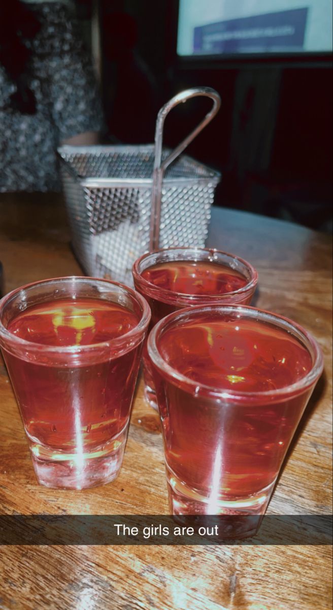 three shot glasses filled with liquid sitting on top of a wooden table next to a basket