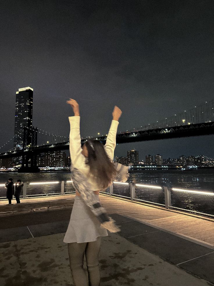 a woman standing on top of a sidewalk next to a river under a dark sky