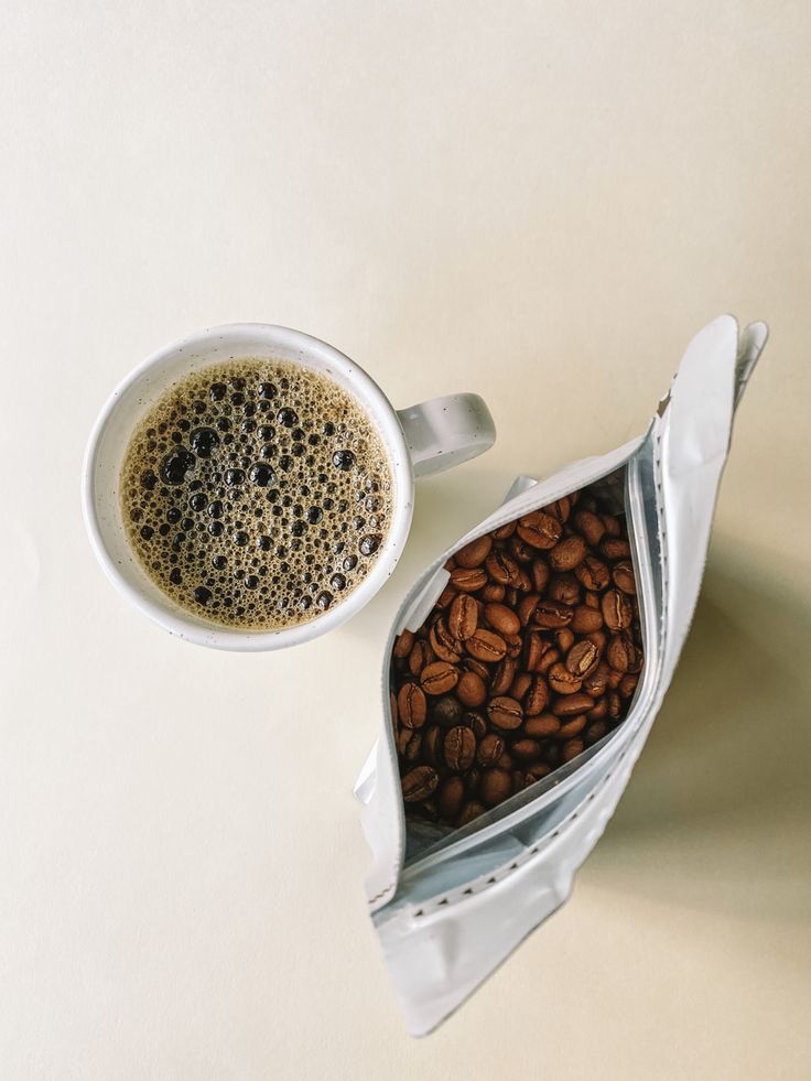 a cup of coffee sitting next to a bag filled with coffee beans