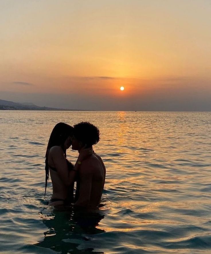 two people are kissing in the water at sunset