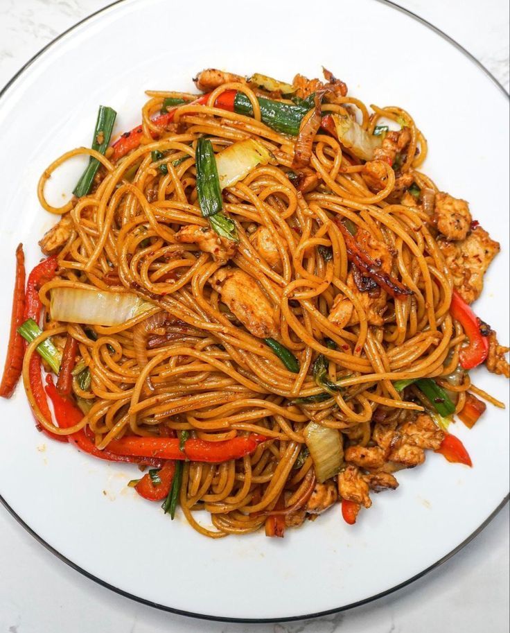 a white plate topped with stir fry noodles and vegetables on top of a marble table