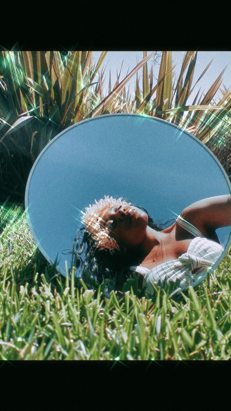 a woman laying on the grass in front of a mirror