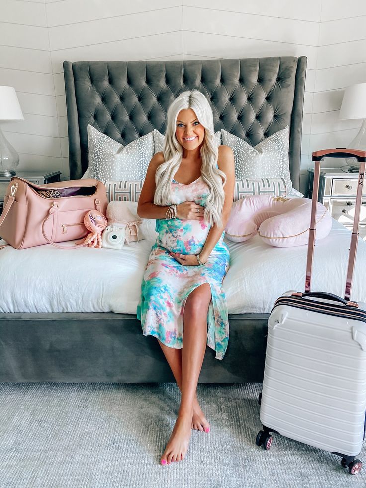 a woman sitting on a bed with her luggage in front of her and smiling at the camera