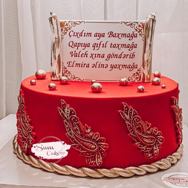 a red and gold decorated cake sitting on top of a white tablecloth covered table