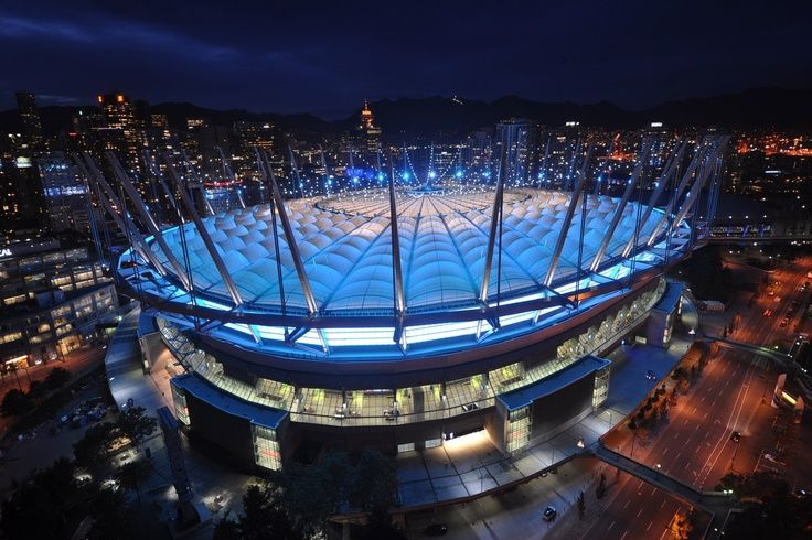 the stadium is lit up at night with blue lights on it's roof and surrounding buildings