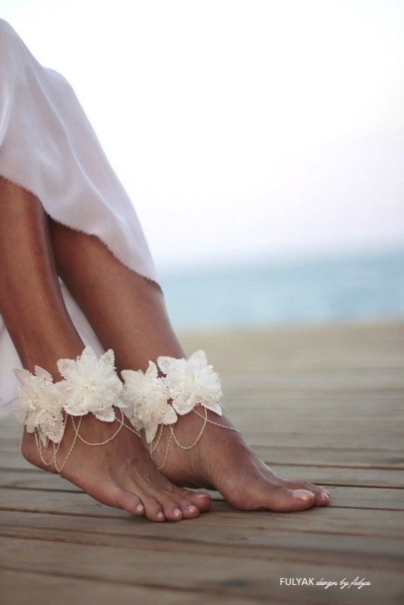 a woman wearing barefoot sandals with white flowers on them sitting on a wooden floor next to the ocean