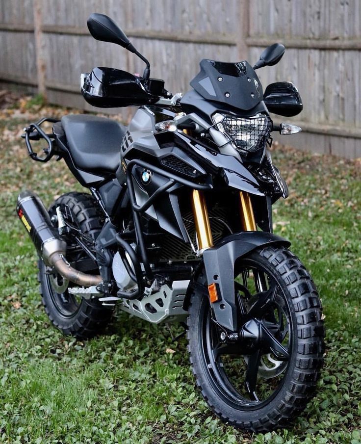 a black motorcycle parked in the grass next to a wooden fence and some green grass