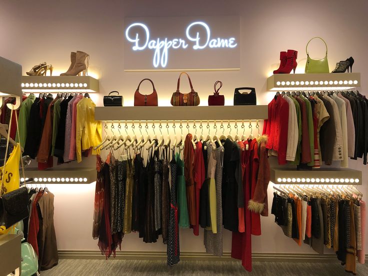 clothes and handbags are displayed on shelves in a clothing store, with neon lights above them