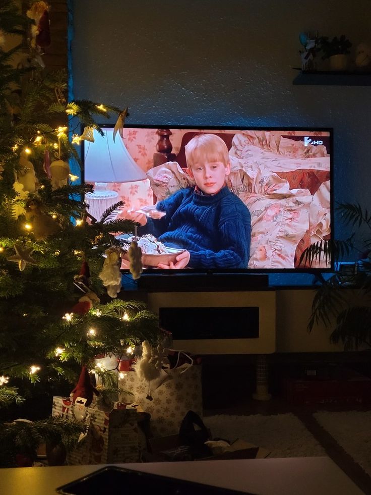 a christmas tree is in front of a television with a boy on it's screen