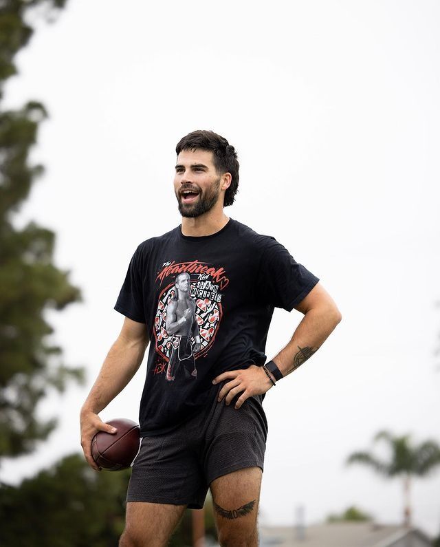 a man holding a football in his right hand and smiling at the camera while standing on a field