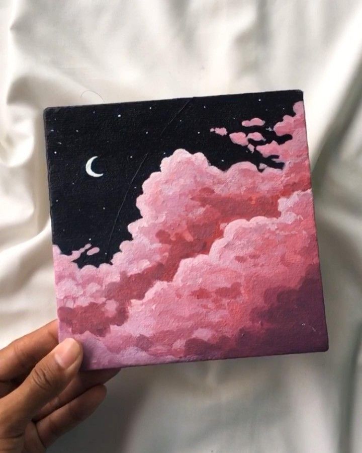 a person holding up a painting with clouds and the moon in the sky above them