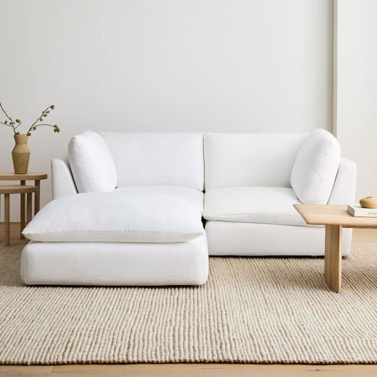 a white couch sitting on top of a rug next to a wooden table and vase