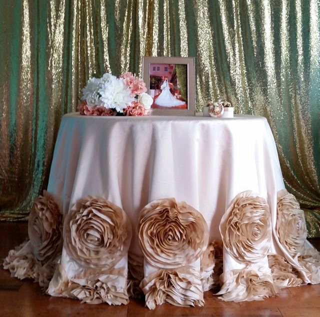 a table topped with a white table cloth covered in ruffles and flowers next to a gold sequin backdrop