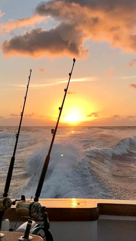 two fishing rods sitting on top of a boat near the ocean as the sun sets