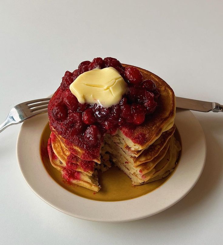 a stack of pancakes topped with raspberries and butter