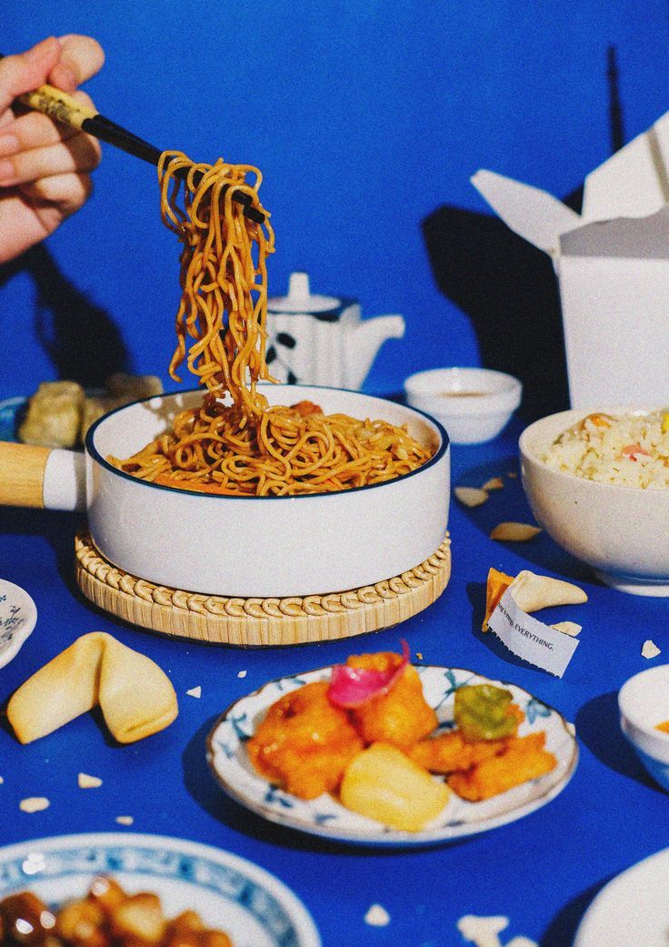 a person is eating noodles with chopsticks at a table full of plates and bowls