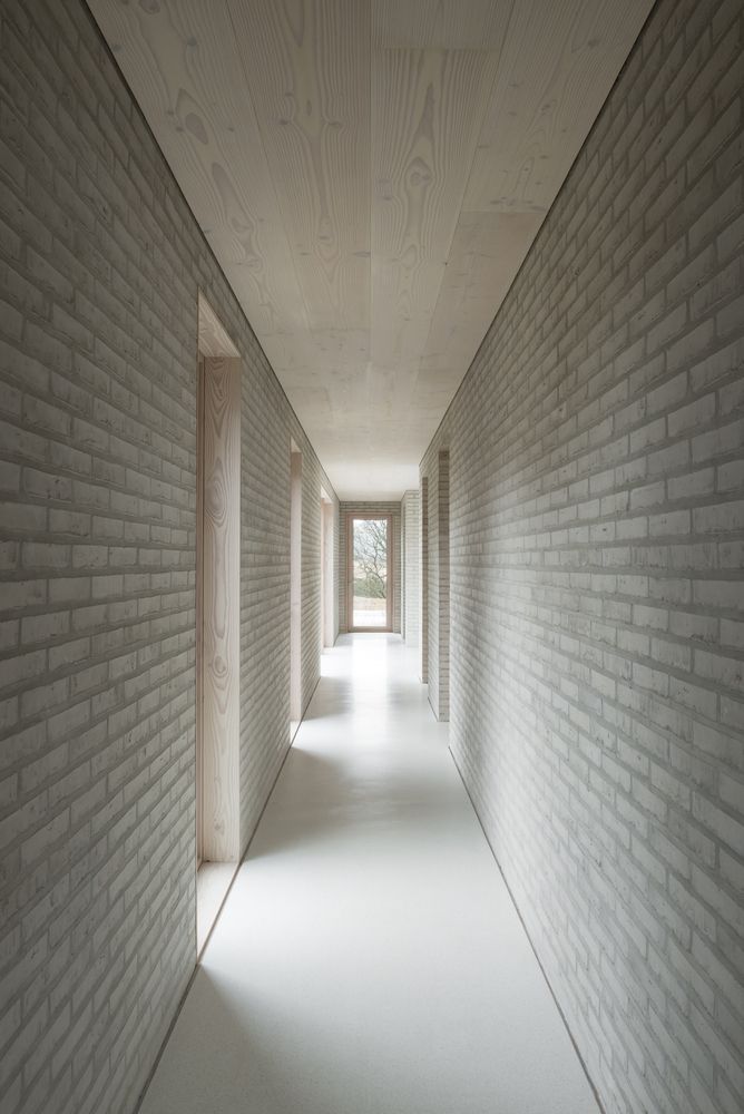 an empty hallway with white brick walls and light coming in from the window at the end