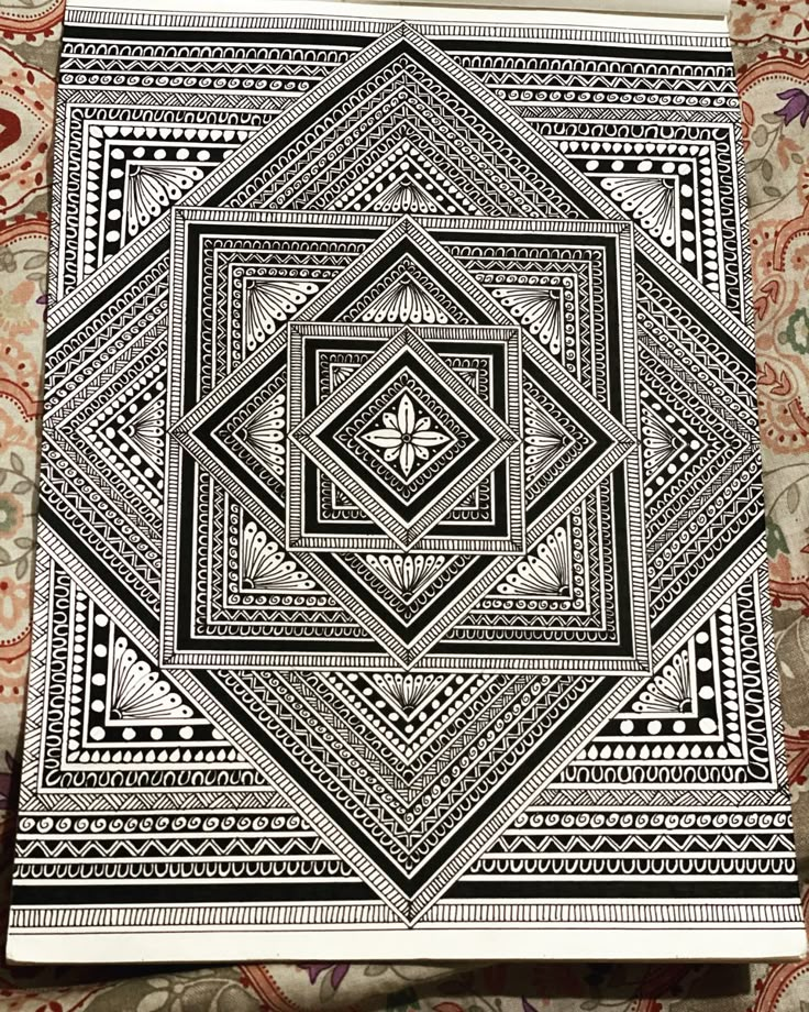 a black and white drawing on paper with an intricate design in the middle, sitting on a patterned surface