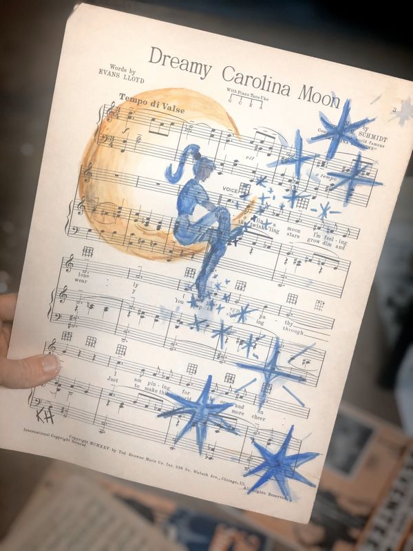 a person holding up a sheet of music with blue stars on it and the words dreamy carolina moon