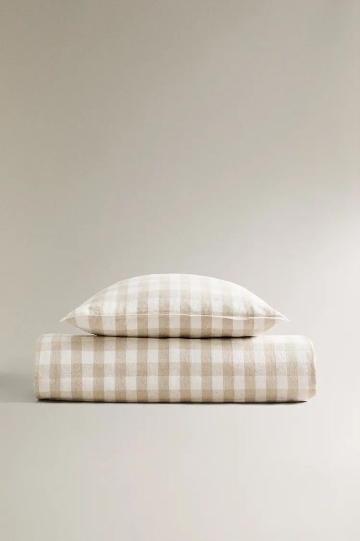 two pillows sitting on top of each other in front of a gray wall with white checkered sheets