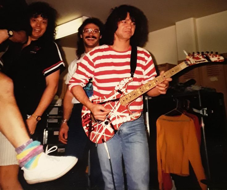 two men are playing guitar while another man is standing next to them with his headphones on