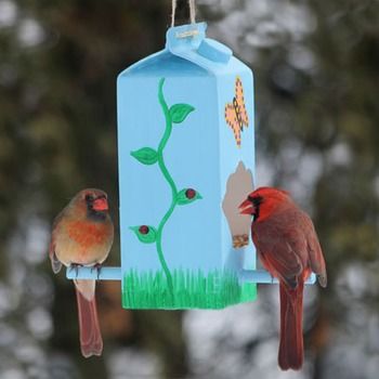 two birds are perched on a bird feeder outside in the snow, one is red and the other is blue