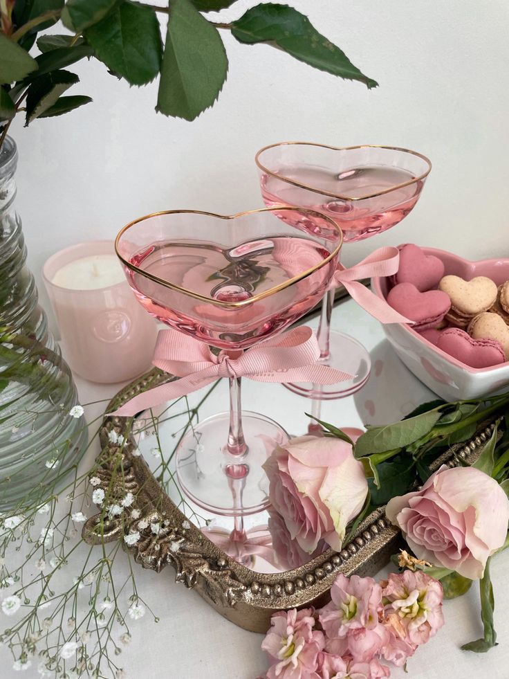 two martini glasses filled with pink wine and candy on a table next to some flowers