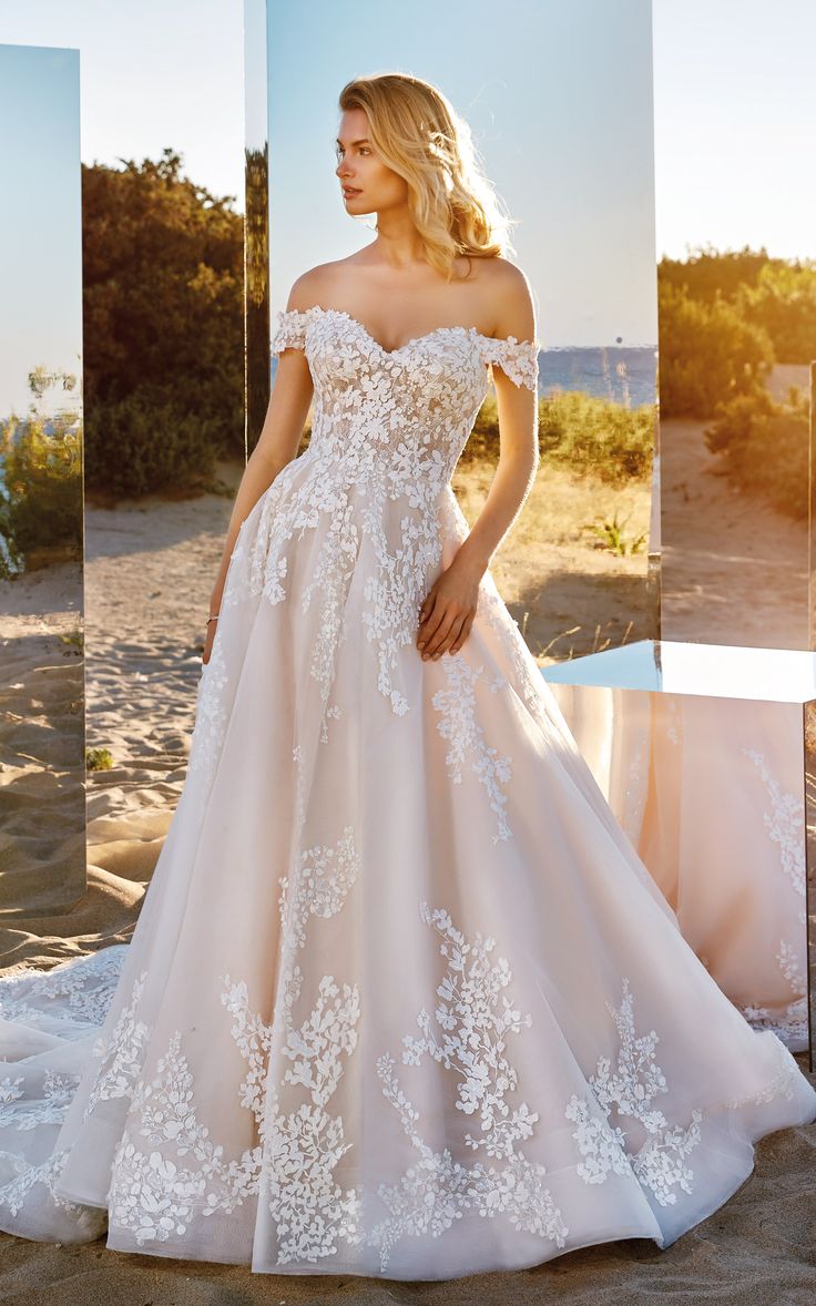 a woman in a wedding dress standing on the beach with her hand on her hip