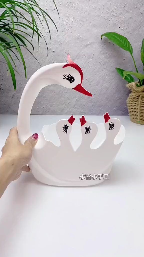 a white swan shaped bowl with red and black designs on it's head, held up by a woman's hand