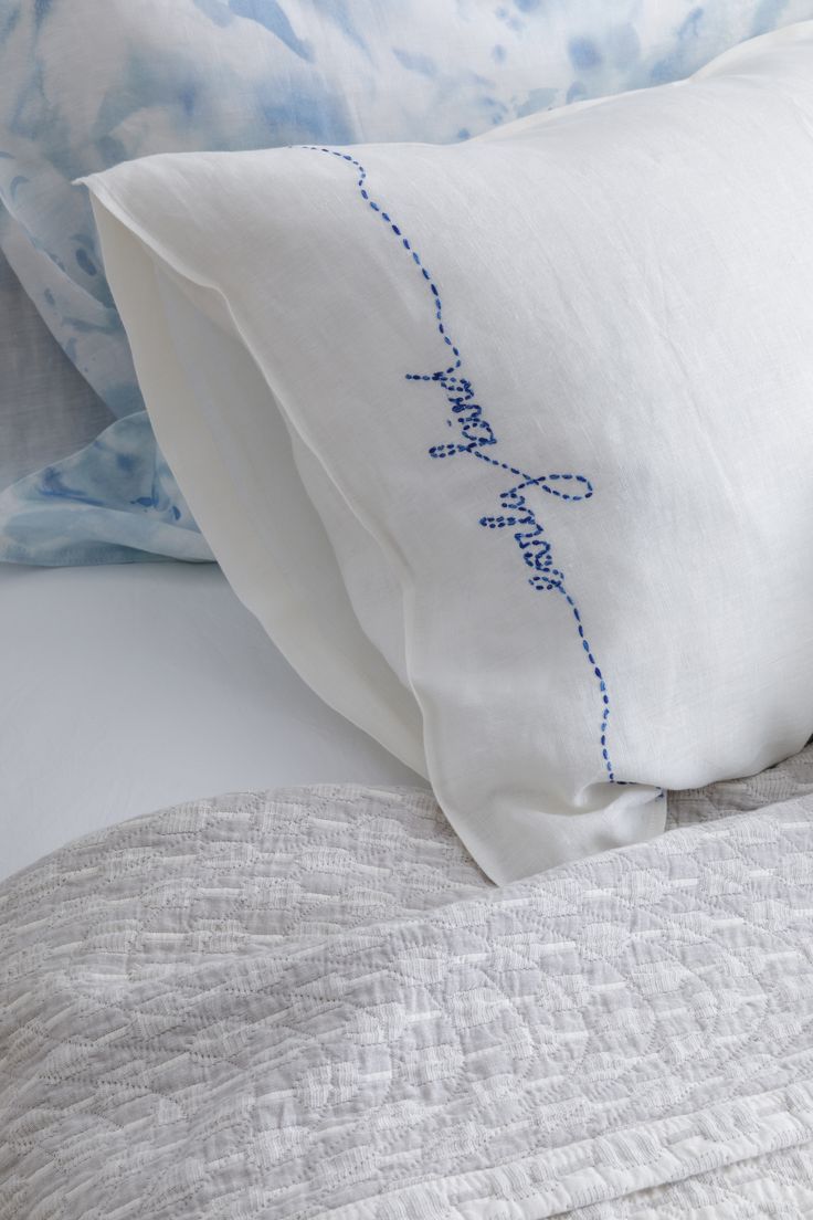 two pillows on top of a bed with blue and white linens in the background