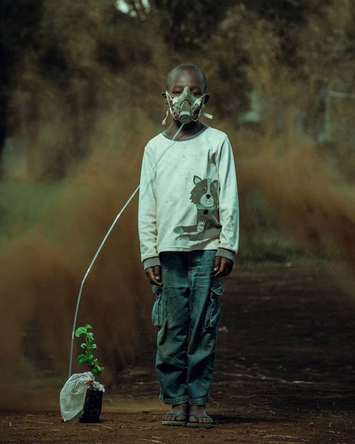 a man wearing a face mask standing in the dirt with a small tree growing out of it