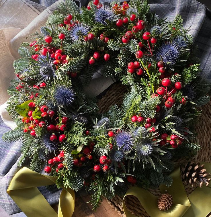 a wreath with red berries, green leaves and pine cones sits on a plaid blanket