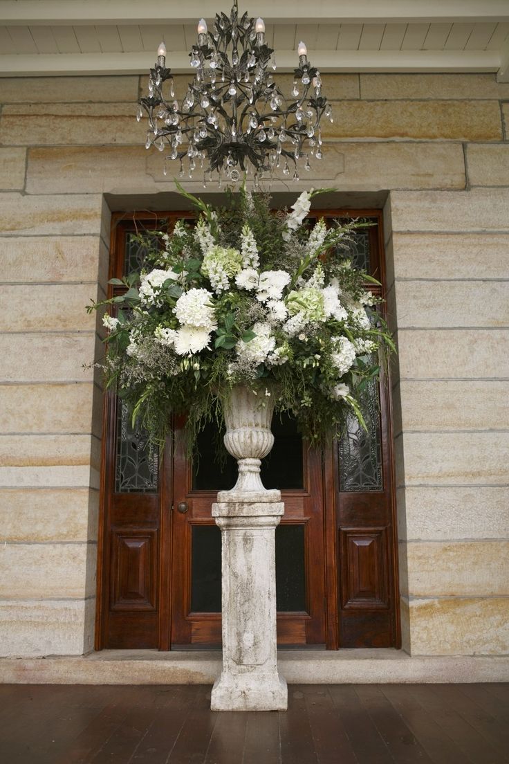 a large vase with flowers in front of a door and chandelier hanging from the ceiling