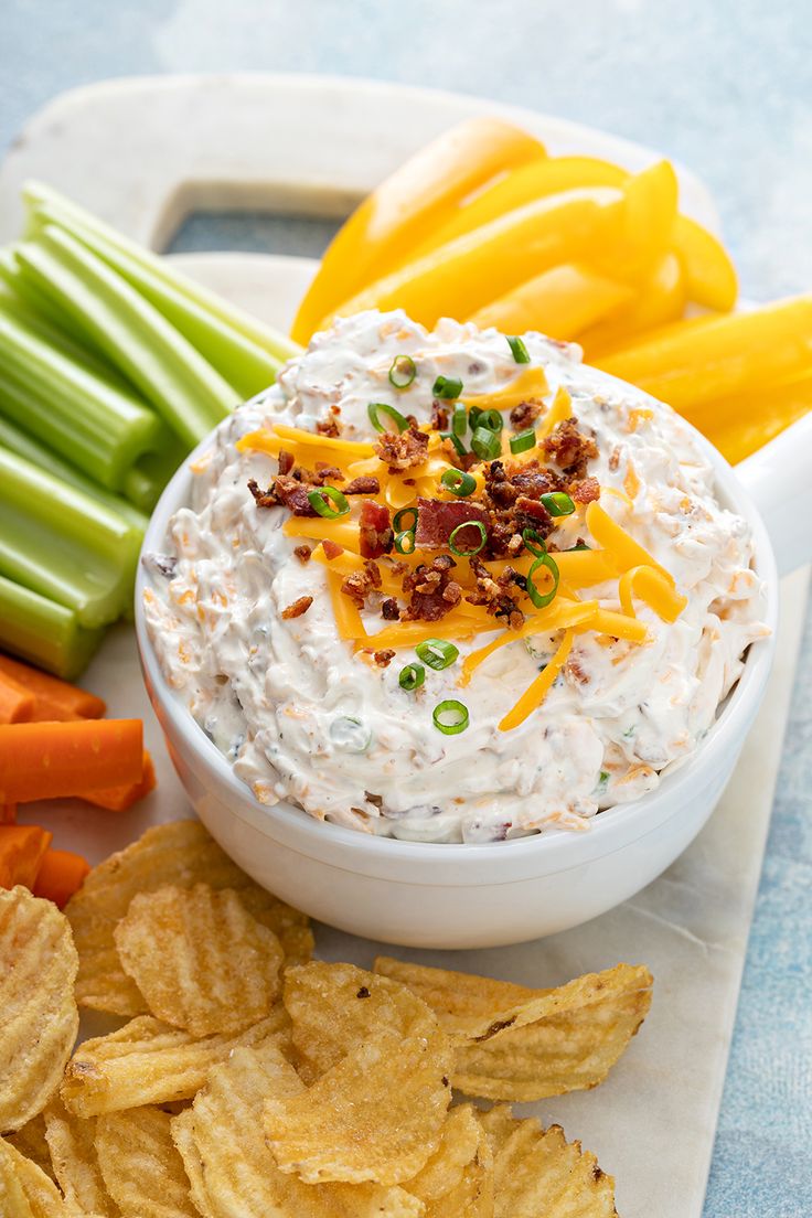 a bowl of dip surrounded by chips and vegetables