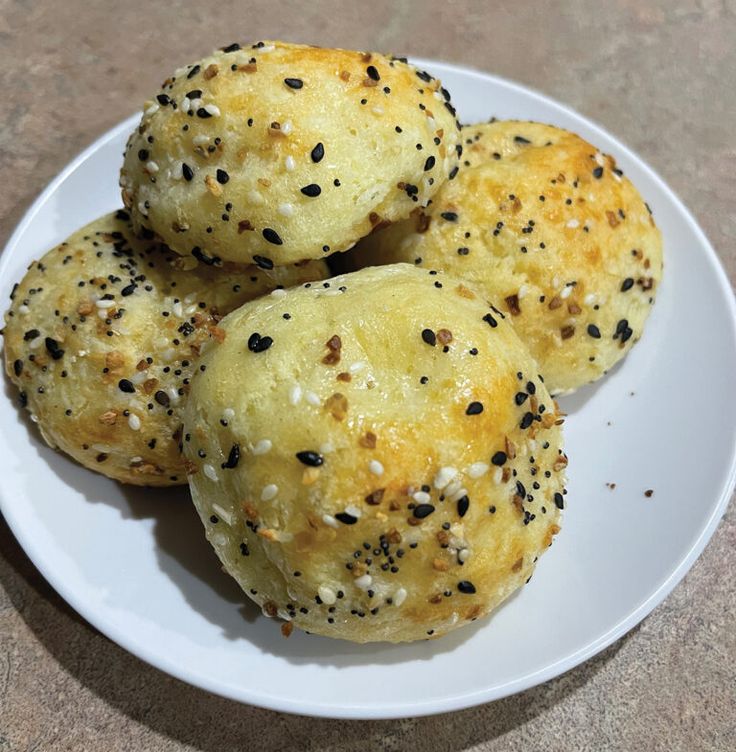 four sesame seed muffins on a white plate