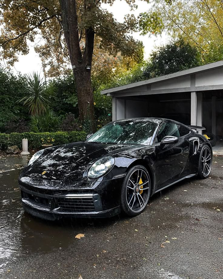 a black sports car parked in front of a garage on a rainy day with no one around