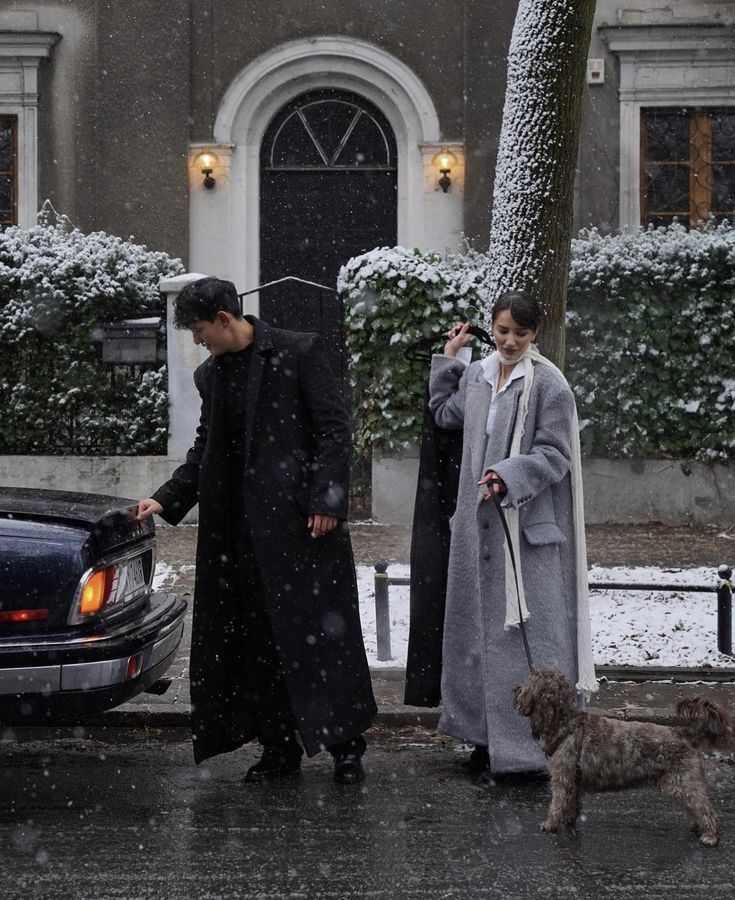 a man and woman walking their dog in the snow while they are dressed for winter