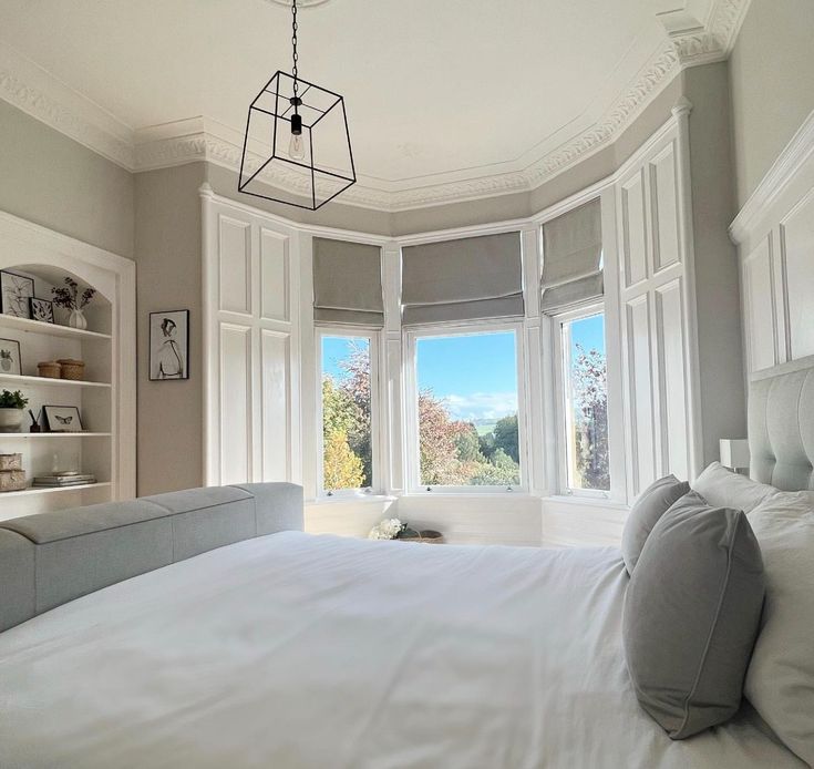 a large white bed sitting in a bedroom next to a window filled with lots of windows