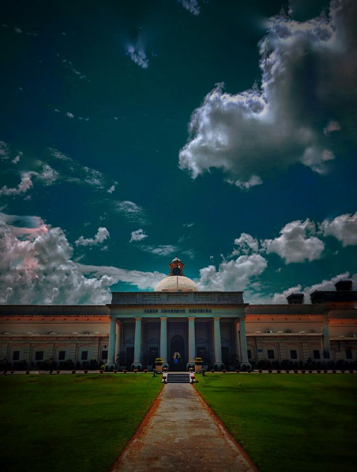 a large building sitting on top of a lush green field under a cloudy blue sky