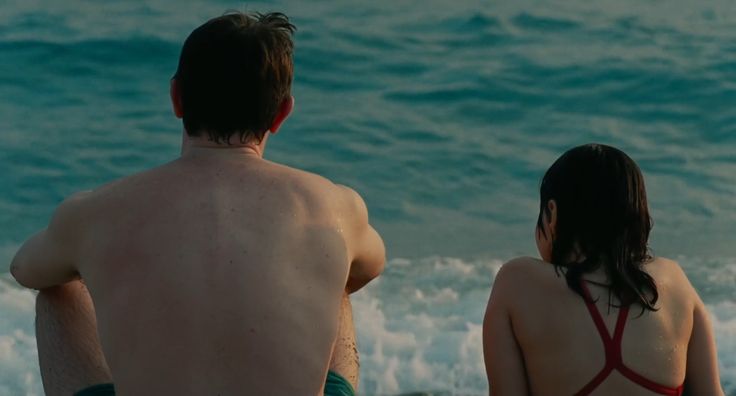 two people sitting on the beach looking out at the ocean