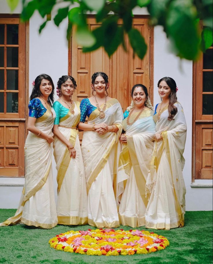 a group of women standing next to each other in front of a doorway with flowers on the ground