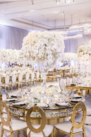 the tables are set with white flowers and gold chairs