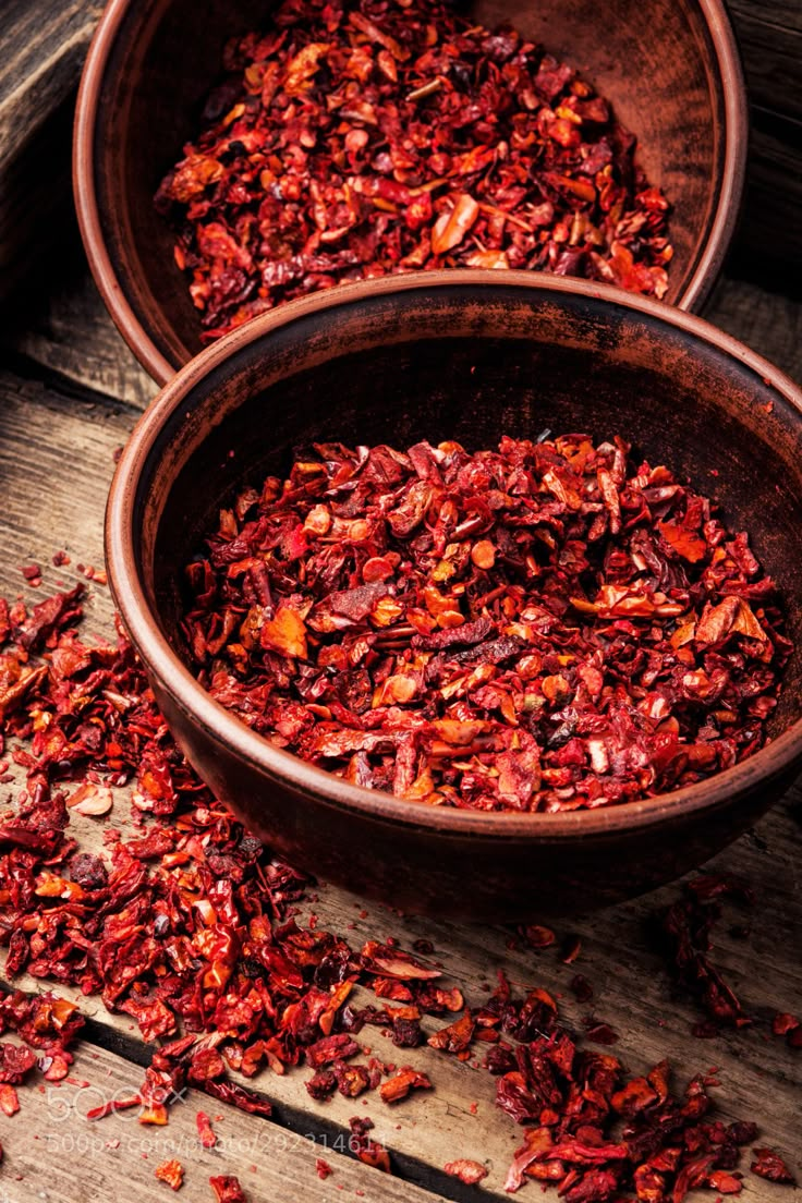 two bowls filled with dried red flowers on top of a wooden table