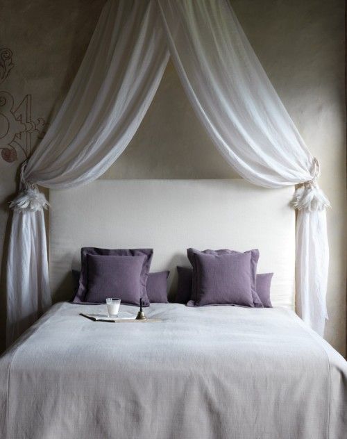 a bed with white drapes and purple pillows