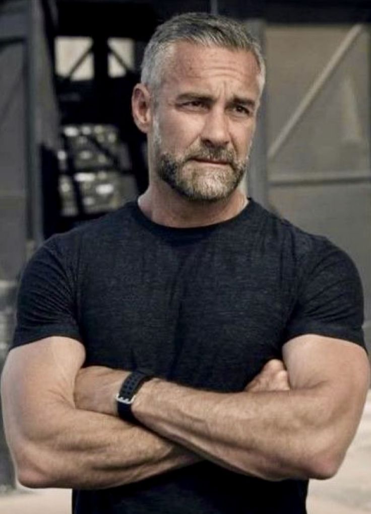 a man standing with his arms crossed and looking at the camera while wearing a black t - shirt