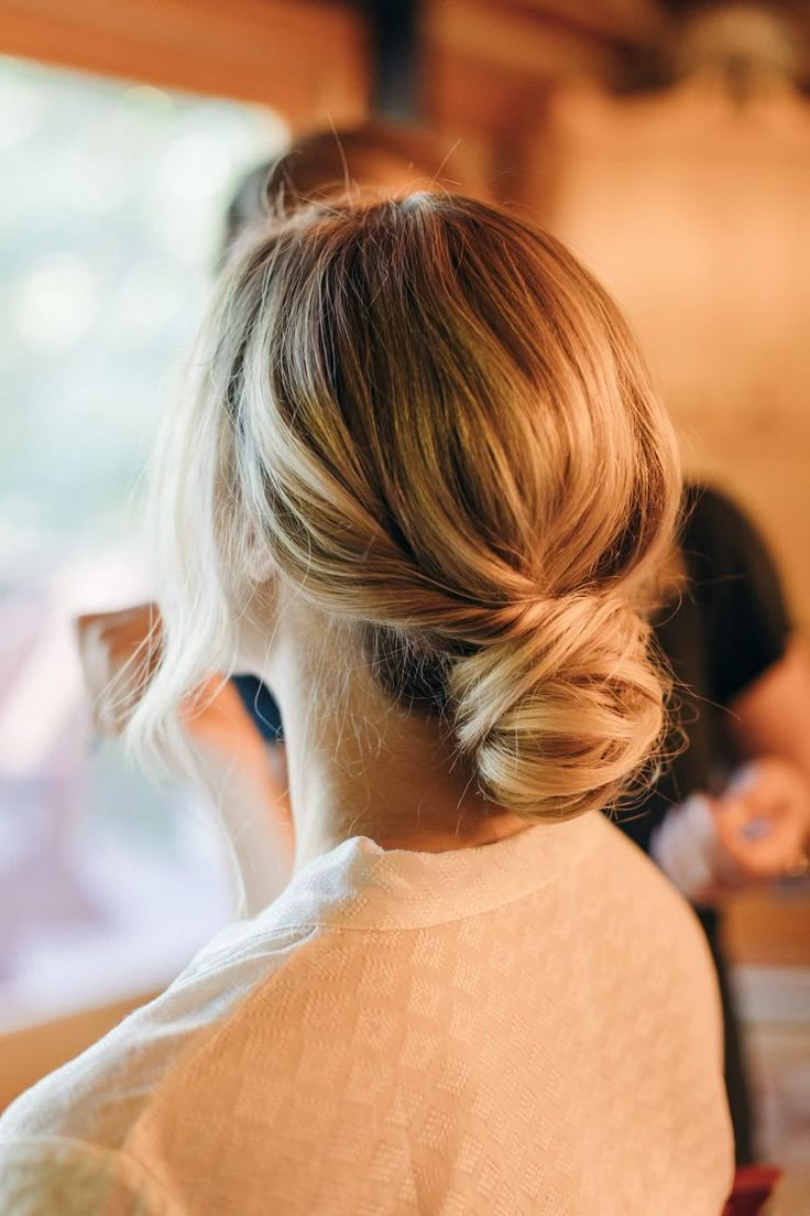 a woman with her hair in a low bun is looking out the window at another person