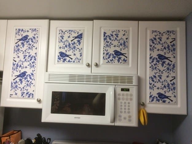 a white microwave oven sitting inside of a kitchen next to cabinets with blue birds on them