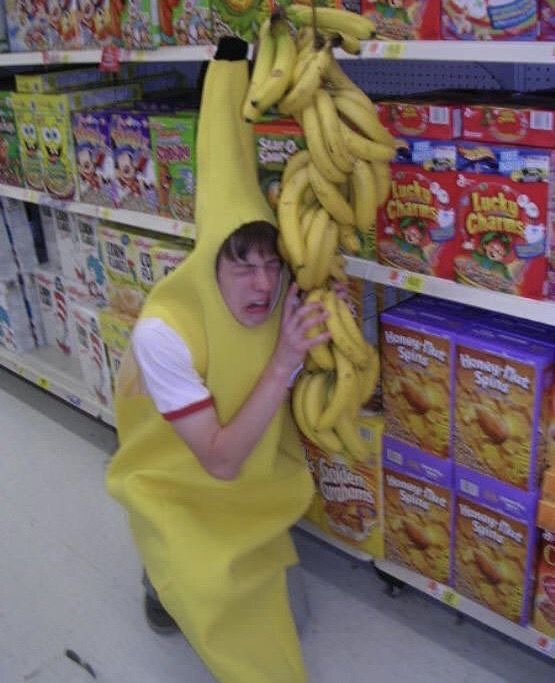 a boy in a banana suit is holding on to a bunch of bananas at the grocery store