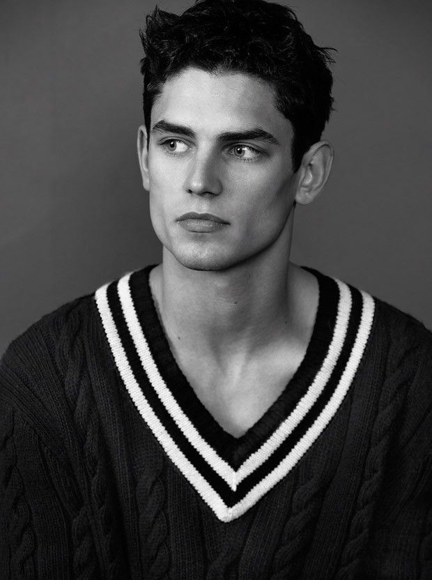 black and white photograph of a young man wearing a v - neck sweater, looking at the camera