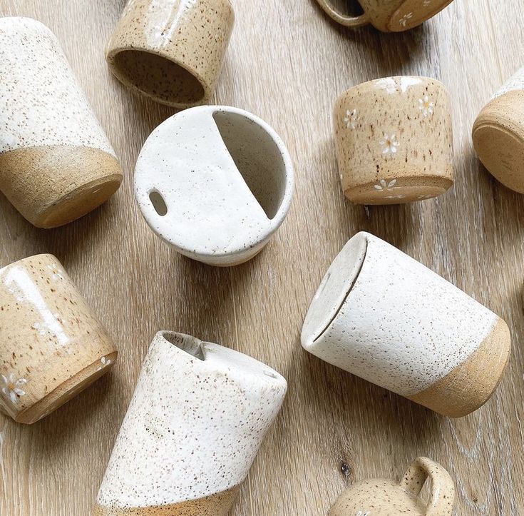 several ceramic cups sitting on top of a wooden table next to each other and one cup with holes in the middle